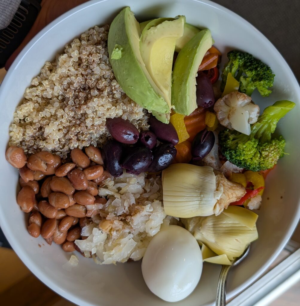 bowl of food containing eggs, quinoa, sauerkraut, artichoke hearts, avocado, cruciferous vegetables and kalamata olives